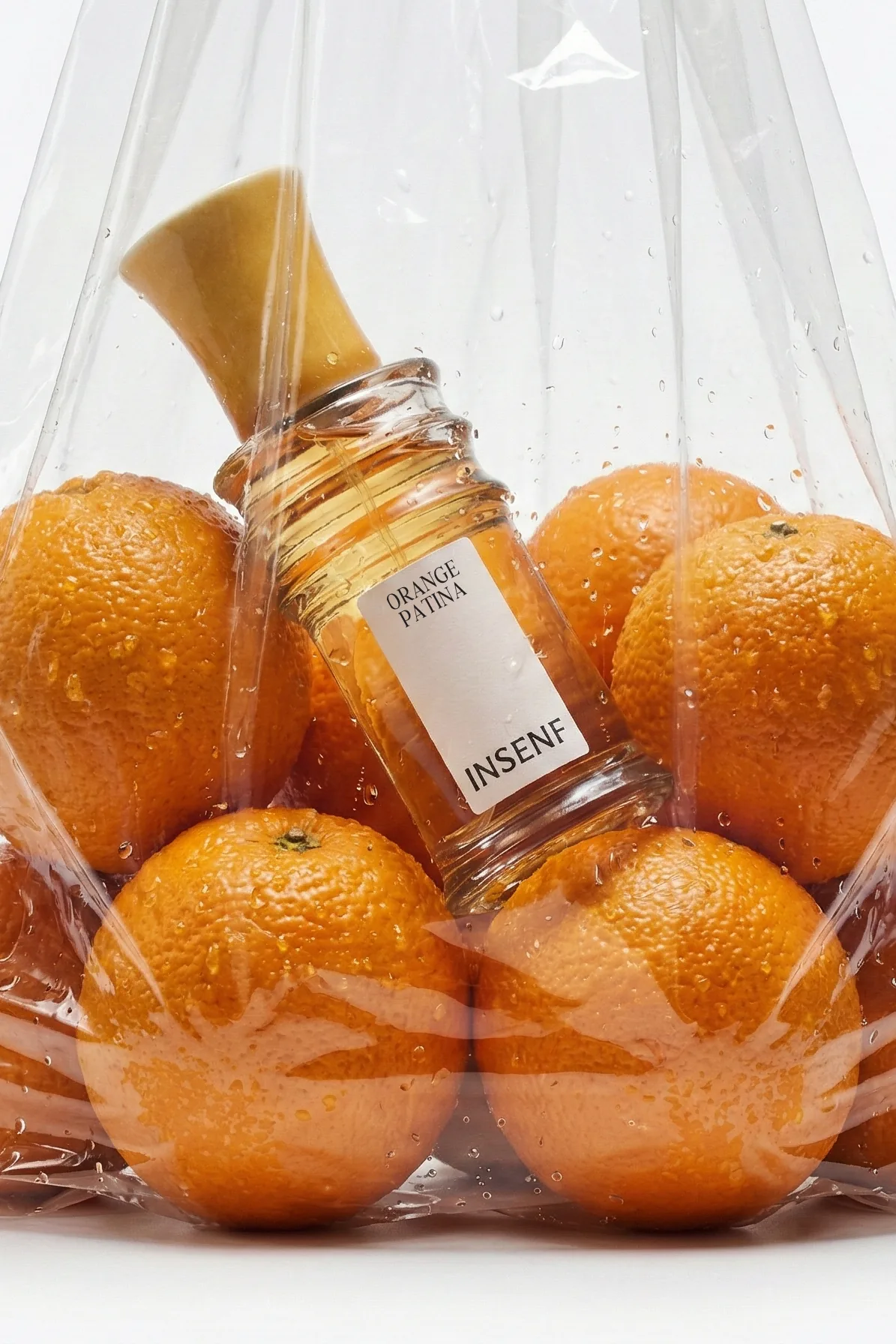 Orange Patina, INSENF — flacon entouré d'oranges dans un sac translucide