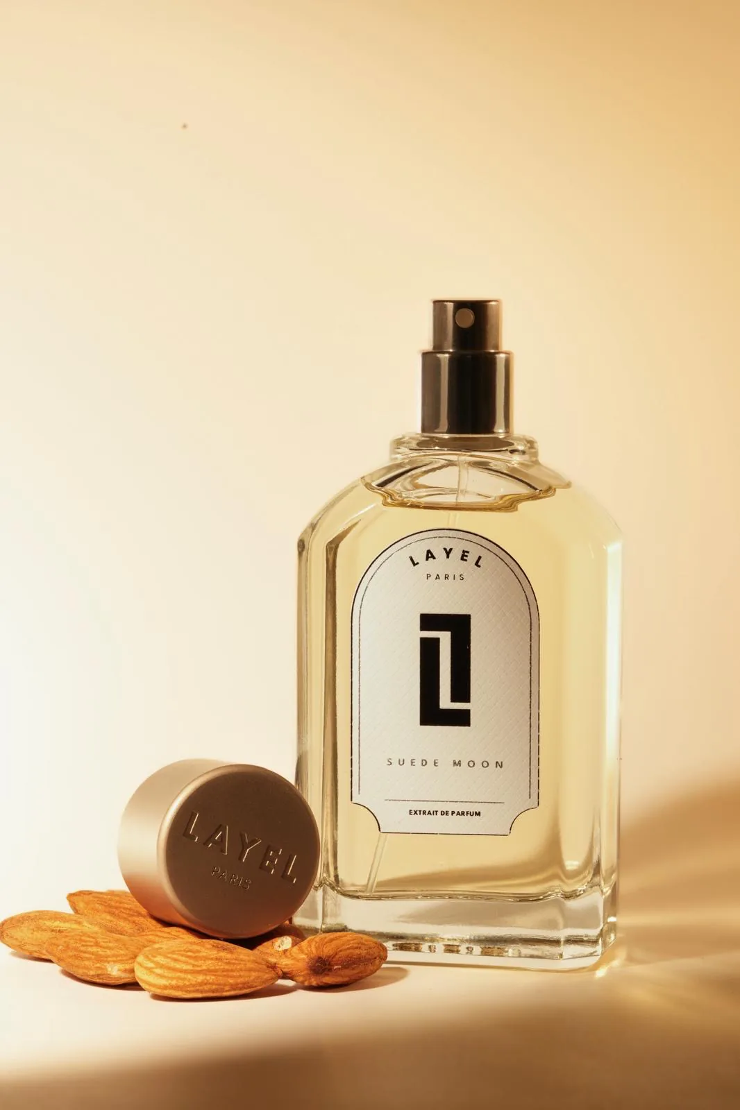 Suede Moon, LAYEL PARIS — flacon ambré, amandes et bouchon gravé sur fond crème