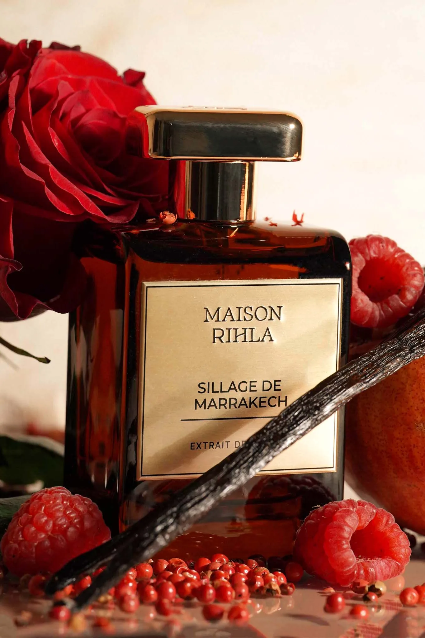 Sillage de Marrakech, flacon ambré devant une grenade ouverte et une rose